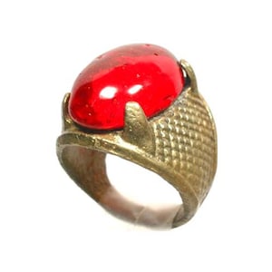 Puede incluir: Un anillo de latón con una piedra de vidrio roja engastada en un diseño de corona.