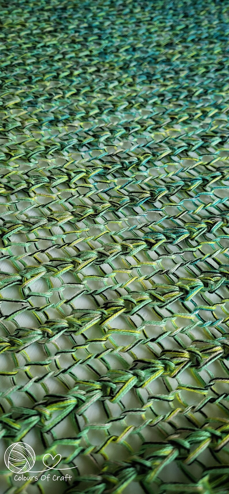 Op de afbeelding: Een close-up van een groene, blauwe en gele gehaakte stof met een zwarte draad die er doorheen geweven is. De stof is gemaakt met een herhalend patroon van knopen en lussen.