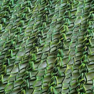 Op de afbeelding: Een groene en gele gehaakte stof met een geweven patroon. De stof is gemaakt van dik garen en heeft een losse, open weving.