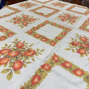 May include: A white tablecloth featuring a repeating pattern of orange fruit and green leaves. The design alternates between square frames composed of oranges and foliage and clusters of oranges with leaves arranged in a grid across the fabric.