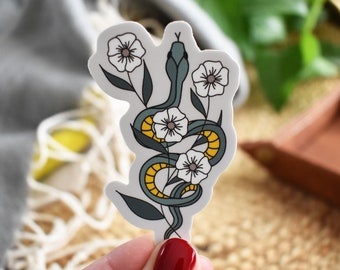 Può includere: Un adesivo con un serpente verde con accenti gialli, avvolto attorno a fiori bianchi con centri gialli. Il serpente e i fiori sono su uno sfondo bianco.