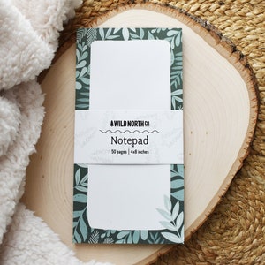 May include: A green and white notepad with a leafy design and the text "WILD NORTH CO. Notepad 50 pages | 4x8 inches" on the front.