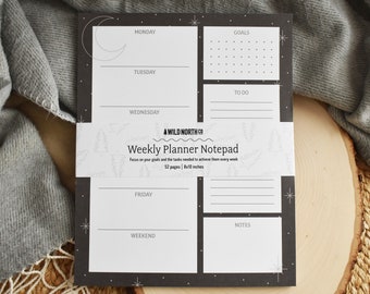 May include: A black and white weekly planner notepad with a moon and stars design. The notepad has sections for Monday, Tuesday, Wednesday, Friday, Weekend, Goals, To Do, and Notes. It also says "A Wild North Co. Weekly Planner Notepad" and "52 pages | 8x10 inches".