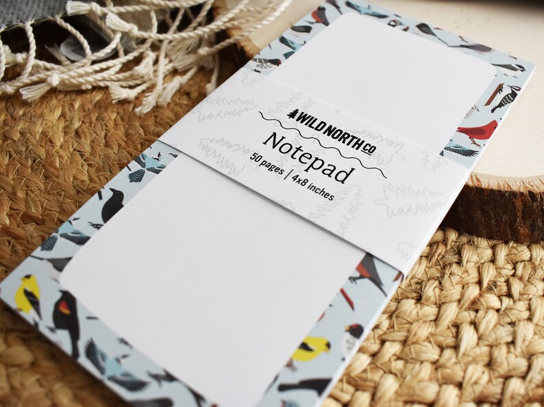 Puede incluir: Un bloc de notas con un patr&oacute;n de p&aacute;jaros azul y blanco en la portada. El bloc de notas tiene 50 p&aacute;ginas y mide 10,2x20,3 cm. El texto en la portada dice "Wild North Co. Notepad 50 pages | 4x8 inches".