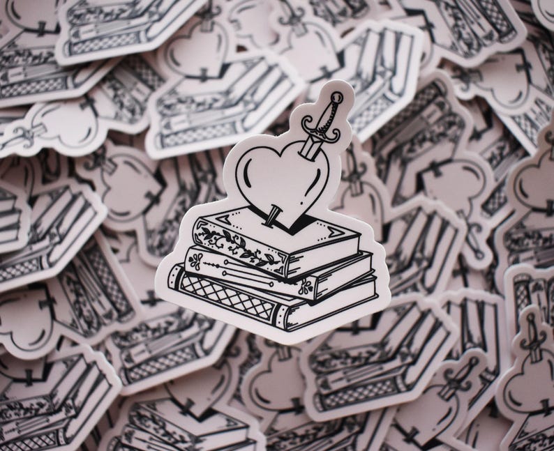 May include: A black and white illustration of a stack of books with a heart pierced by a dagger on top. The heart is surrounded by a white background.