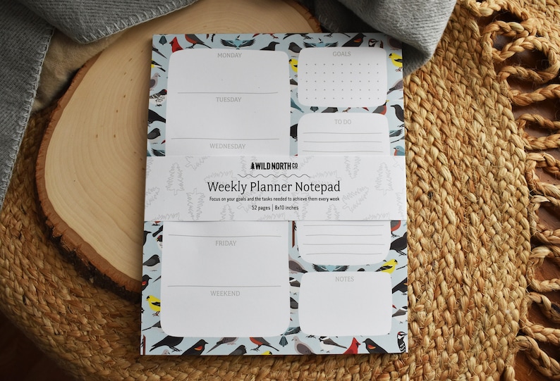 Puede incluir: Un bloc de notas azul con un patr&oacute;n de p&aacute;jaros y el texto "#WILD NORTH CO Weekly Planner Notepad Focus on your goals and the tasks needed to achieve them every week 52 pages | 8x11 inches"