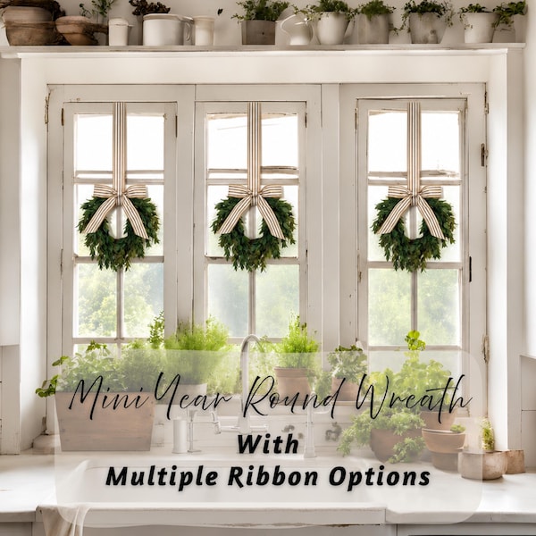 May include: Three small green wreaths hanging on a white window frame, each adorned with a beige and white striped ribbon tied in a bow. The text "Mini Year Round Wreath With Multiple Ribbon Options" is overlaid in black script and print font.