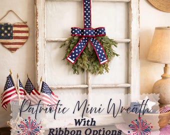 May include: A rustic white wooden window frame featuring a green wreath hung by a navy blue ribbon with white stars. The display includes a heart-shaped American flag sign, small American flags in a bucket, and text reading Patriotic Mini Wreath With Ribbon Options.