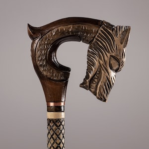 May include: A wooden walking stick with a carved wolf head handle. The handle is brown and the stick is brown with a copper band and a white and black checkered pattern.