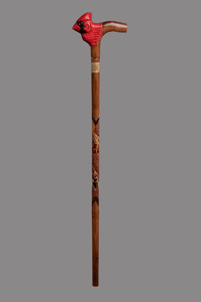 May include: A wooden walking stick with a carved cardinal head at the top. The stick is decorated with intricate carvings of flowers and leaves.