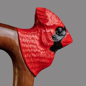 May include: A wooden walking stick with a carved cardinal head handle. The cardinal is painted red with black accents for the eyes and beak.
