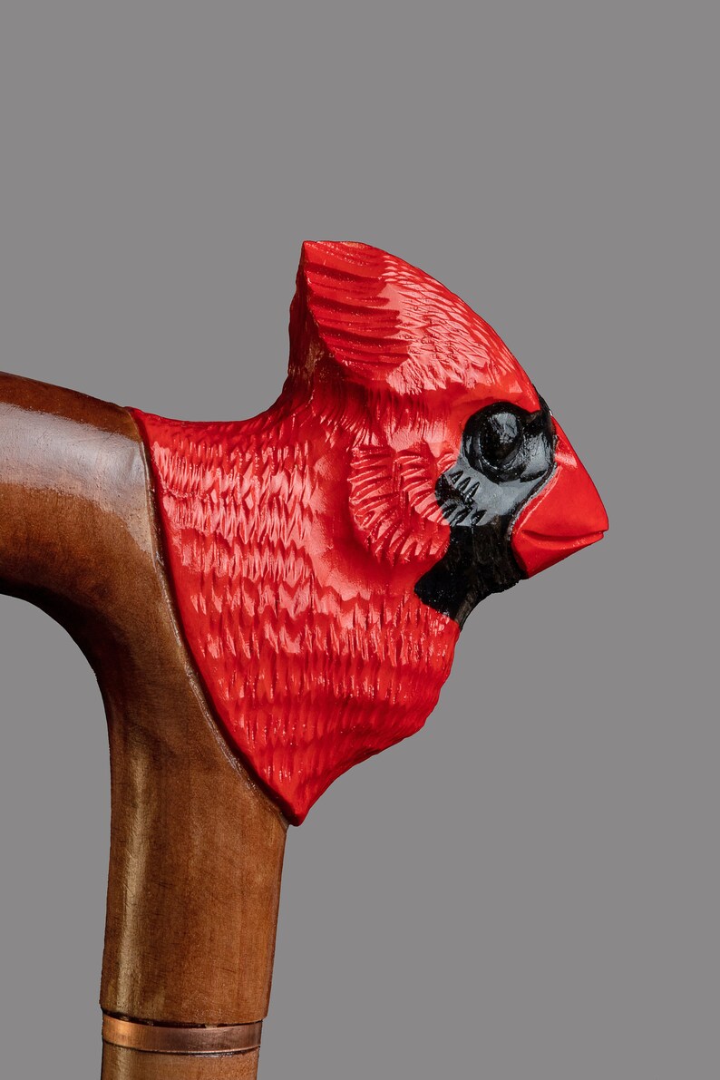 May include: A wooden walking stick with a carved cardinal head handle. The cardinal is painted red with black accents for the eyes and beak.