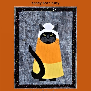 May include: A Halloween-themed quilt featuring a black cat dressed as candy corn. The cat has a white and black head, an orange and yellow body, and a long black tail. The background is gray with a spider web and a small spider. Text reads "Trouble & Boo Designs" and "Kandy Korn Kitty."