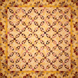 May include: A quilt with a geometric pattern of yellow, brown, and pink squares and triangles. The quilt is surrounded by a border of floral fabric.