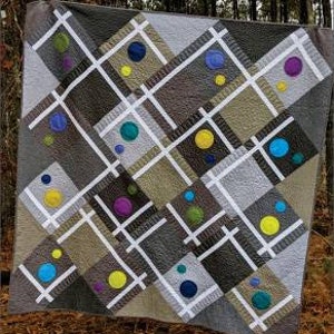May include: A quilt pattern called "Fractions" by Swirly Girls. The pattern features a grid of squares with circles of various colors and sizes. The text "Fractions is great for solids or feature your favorite prints!" is at the bottom of the image.