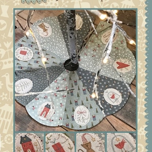 May include: A handmade Christmas tree skirt with a patchwork design featuring a variety of holiday-themed fabrics. The skirt is made in a blue and gray color scheme with red accents. The skirt is decorated with various embroidered designs, including houses, birds, and a cat. The text "The Giving Tree Skirt" is printed at the bottom of the image.