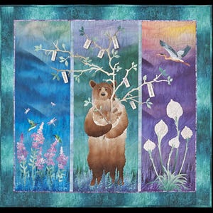 May include: A fabric wall hanging quilt featuring a central brown bear holding a white tree branch with tags labeled Honor, Protect, Enjoy, Save, Conserve, Love, Care, and Preserve. The scene includes hummingbirds, dragonflies, and a bird in flight.