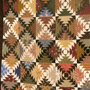 May include: A quilt made of various fabrics in shades of brown, green, white, and red. The quilt is made up of a repeating pattern of pineapples, each made up of smaller triangles. The quilt is a traditional design and is a beautiful example of handmade craftsmanship.