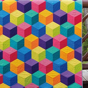May include: A colorful quilt with a geometric pattern of cubes in shades of blue, green, yellow, orange, pink, and purple. The quilt is hanging on a wooden railing with a river in the background. The text "JAYBIRD QUILTS" is visible in the bottom right corner.
