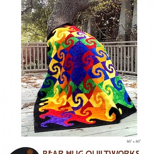 May include: A colorful quilt with a swirling pattern in shades of red, orange, yellow, green, blue, and purple. The quilt is draped over a tree trunk and is 80 inches by 80 inches. The quilt is titled "Twisted" and is a pattern by Bear Hug Quiltworks.