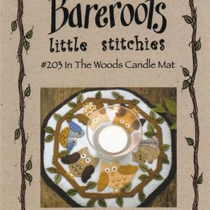 May include: A felt candle mat with a woodland theme. The mat is white with brown branches and leaves, and features various animals including owls, birds, and squirrels. The text "#203 In The Woods Candle Mat" is printed on the image.