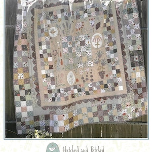 May include: A quilt pattern featuring a patchwork design with a variety of floral motifs and the text "Where Wildflowers Grow". The quilt is hanging on a wooden fence. The pattern is called "Hatched and Patched" and includes contact information for the designer.