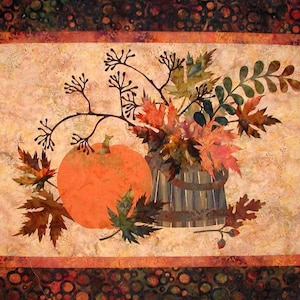 May include: A fall-themed quilt block with a pumpkin, leaves, and a branch in a rustic wooden bucket. The background is a light beige with a subtle pattern.