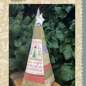 May include: A handmade quilted Christmas tree ornament in the shape of a cone. The ornament is made of various fabrics in shades of green, red, blue, and white. The ornament features a star on top and the text "Merry Christmas" and "Mistletoe and eggnog, plum pudding and turkey, holly and Christmas cheer".