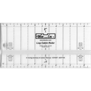 May include: A clear plastic ruler with markings for measuring in inches. The ruler is labeled "Bloc-Loc Log Cabin Ruler" and includes the website address "www.blocloc.com". The ruler has a white strip with the text "In loving memory of Janna Thomas 12/14/57-02/17/24".