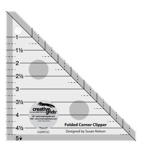May include: A clear plastic ruler with a black outline and markings. The ruler is shaped like a triangle and has a 5-inch scale. The ruler is labeled "Folded Corner Clipper" and "Designed by Susan Nelson".