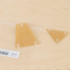 May include: Two clear acrylic Dresden Star templates, labeled A and B, for quilting. The templates are tan and have white markings. The templates are on a light tan surface. A label with text is in the lower left corner.
