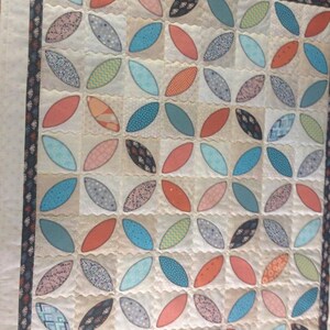 Pode incluir: Uma colcha branca com um padr&atilde;o repetitivo de formas ovais turquesa, azul, laranja e rosa. A colcha &eacute; acolchoada com um padr&atilde;o de pontos ondulados.