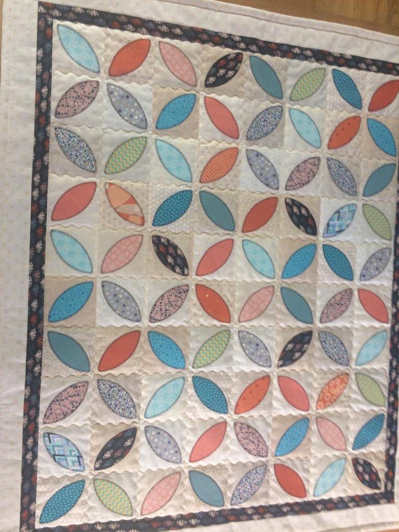 Pode incluir: Uma colcha branca com um padr&atilde;o repetitivo de formas ovais turquesa, azul, laranja e rosa. A colcha &eacute; acolchoada com um padr&atilde;o de pontos ondulados.