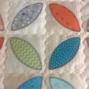 Pode incluir: Um cobertor com uma variedade de padr&otilde;es de tecido em tons de azul, verde, amarelo, laranja e branco. O tecido &eacute; costurado em forma de folha.