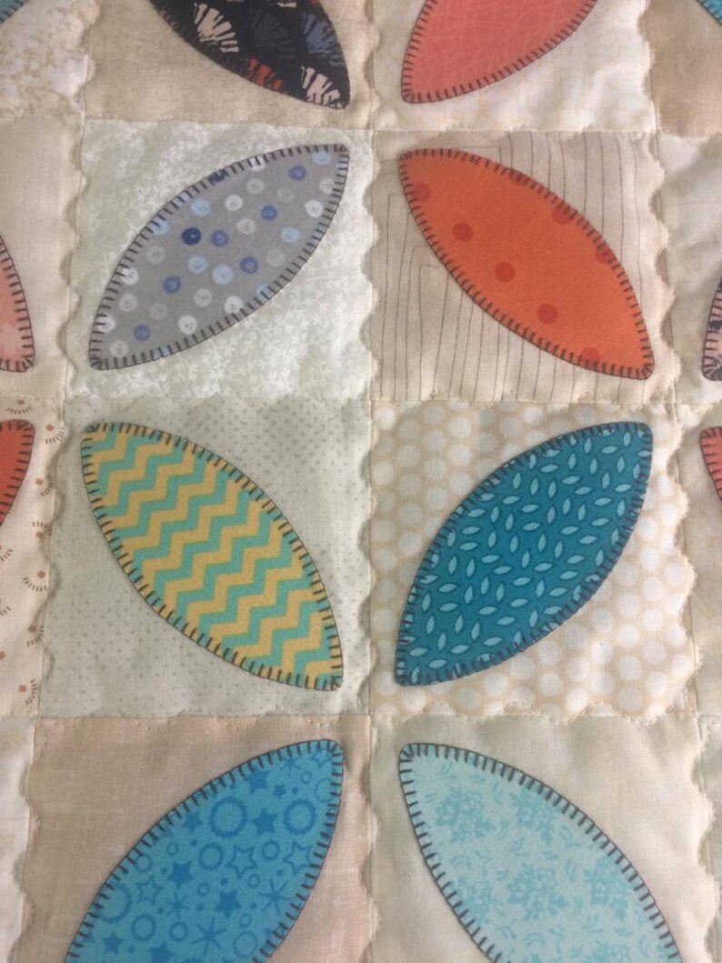 Pode incluir: Um cobertor com uma variedade de padr&otilde;es de tecido em tons de azul, verde, amarelo, laranja e branco. O tecido &eacute; costurado em forma de folha.