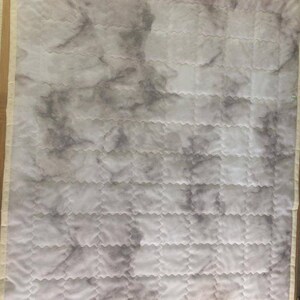 Pode incluir: Uma colcha branca com um padr&atilde;o de m&aacute;rmore cinza. A colcha &eacute; acolchoada em um padr&atilde;o de diamante com uma borda festoneada.