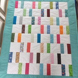 May include: A turquoise blue baby quilt with a white background and colorful fabric strips. The quilt is made with a variety of patterns and colors, including pink, green, blue, orange, and brown.