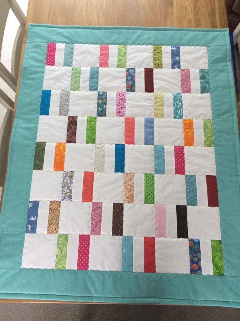 May include: A turquoise blue baby quilt with a white background and colorful fabric strips. The quilt is made with a variety of patterns and colors, including pink, green, blue, orange, and brown.