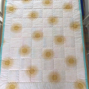 May include: A white quilt with a turquoise border and a repeating pattern of gold suns.