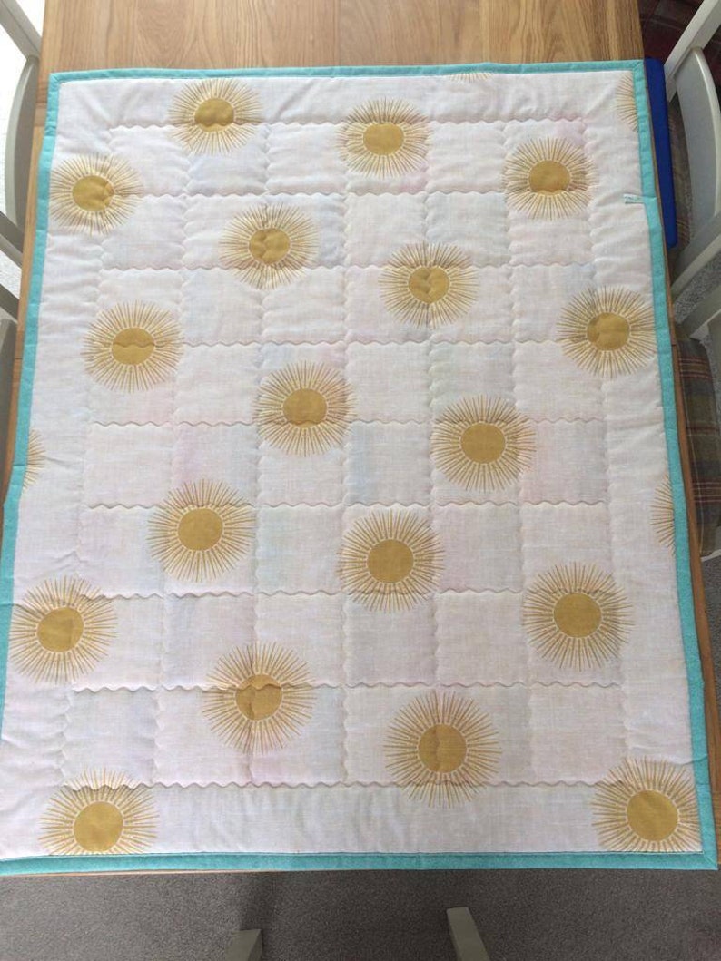 May include: A white quilt with a turquoise border and a repeating pattern of gold suns.