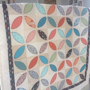 Pode incluir: Uma colcha branca com um padr&atilde;o de folhas turquesa, laranja e rosa. A colcha &eacute; feita de v&aacute;rios tecidos com padr&otilde;es e texturas diferentes.