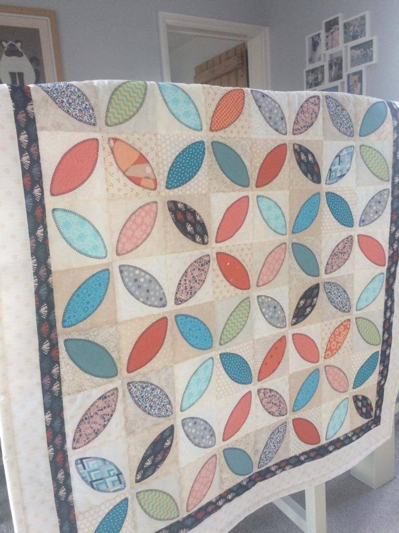 Pode incluir: Uma colcha branca com um padr&atilde;o de folhas turquesa, laranja e rosa. A colcha &eacute; feita de v&aacute;rios tecidos com padr&otilde;es e texturas diferentes.