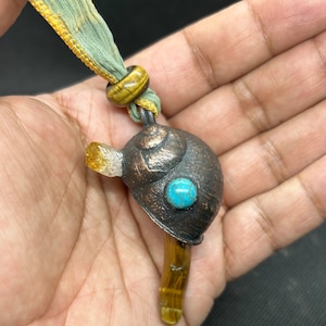 May include: A brown and gold snail charm with a turquoise stone on the shell, hanging from a gold and green ribbon.