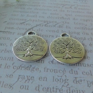 May include: Two silver charm pendants featuring a tree of life design. The tree is stylized with swirling branches and a trunk. The charms are round and have a loop at the top for hanging.