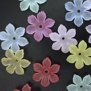 May include: Assortment of pastel colored plastic flower embellishments. The flowers are in shades of pink, blue, yellow, and lavender.