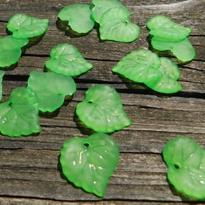 May include: A collection of green glass leaf-shaped beads, scattered on a wooden surface.