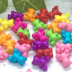May include: A collection of colorful plastic bear-shaped beads. The beads are in various colors, including pink, blue, green, yellow, orange, red, and purple.