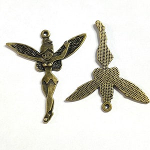 Puede incluir: Dos abalorios de metal de color dorado antiguo, uno con una hada con alas y el otro con una libélula estilizada. Ambos abalorios tienen un bucle para colgar.