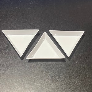 May include: Three white, triangular trays arranged on a dark surface. The trays are empty and have a simple, clean design. These trays are suitable for organizing small items or serving snacks.