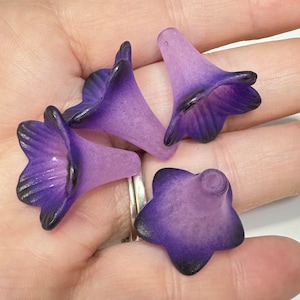 Könnte beinhalten: Vier violette Glasblumenperlen mit mattem Finish. Die Perlen sind glockenförmig mit einer fünfblättrigen Blume oben.